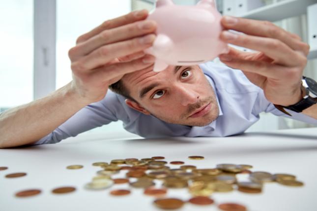 man looking disappointed at the content of emptied piggybank