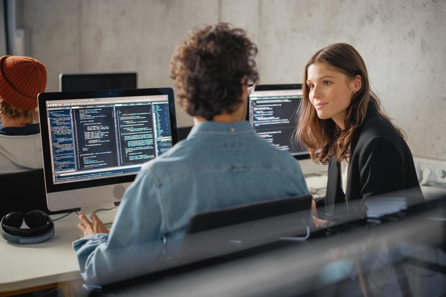 Two people sat together at desk looking at code language on computer